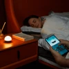 Hand using a smartphone app to control a smart night light next to a sleeping woman in bed
