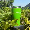 Green Olight stainless steel tumbler with red splatter pattern sitting in lush green bushes outdoors